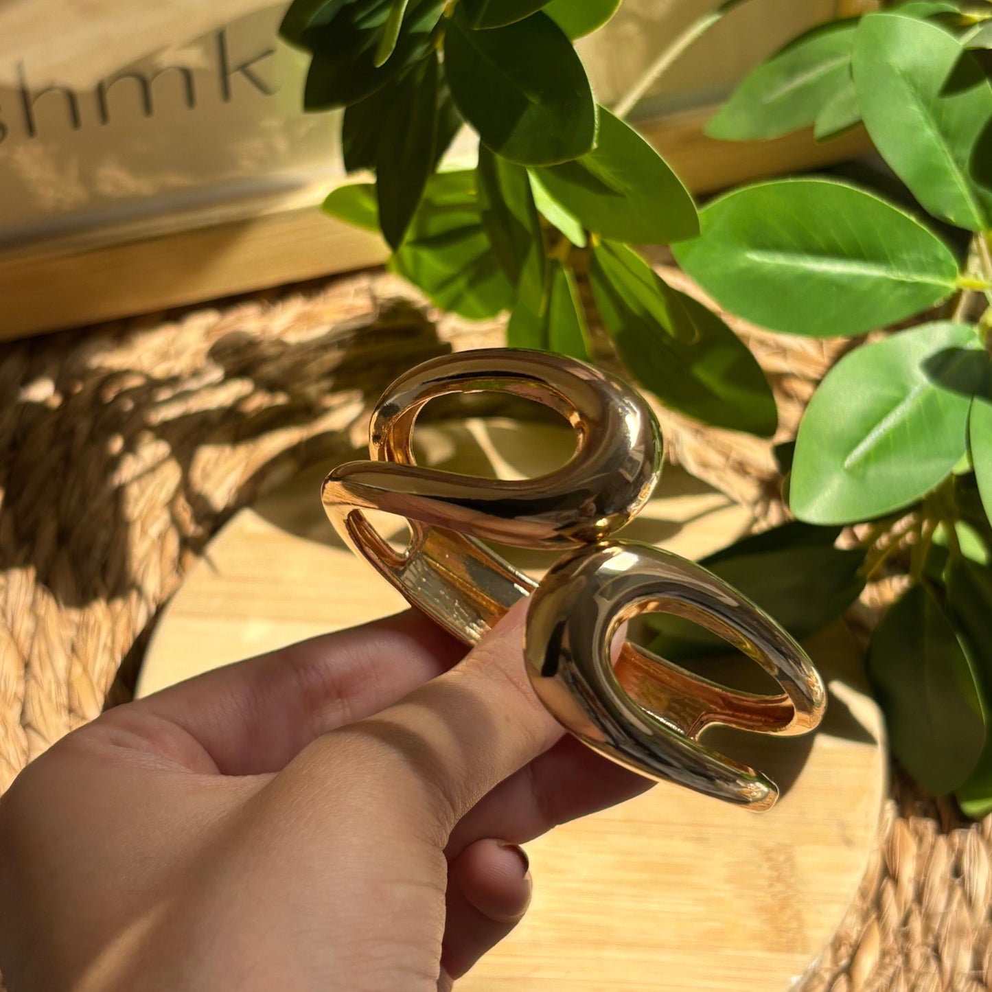 Gold ring held by a hand with a plant and wooden surface in the background
