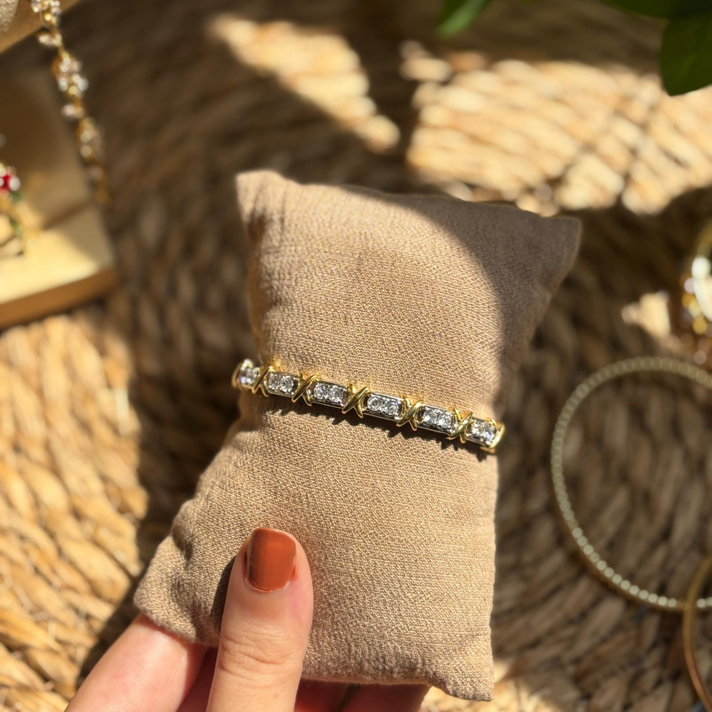 Gold bracelet with diamonds on a beige pillow, held by a hand with orange nail polish.