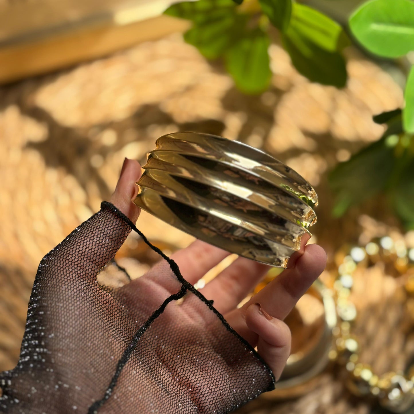 Gold bangles held by a hand wearing a black glove with a blurred natural background