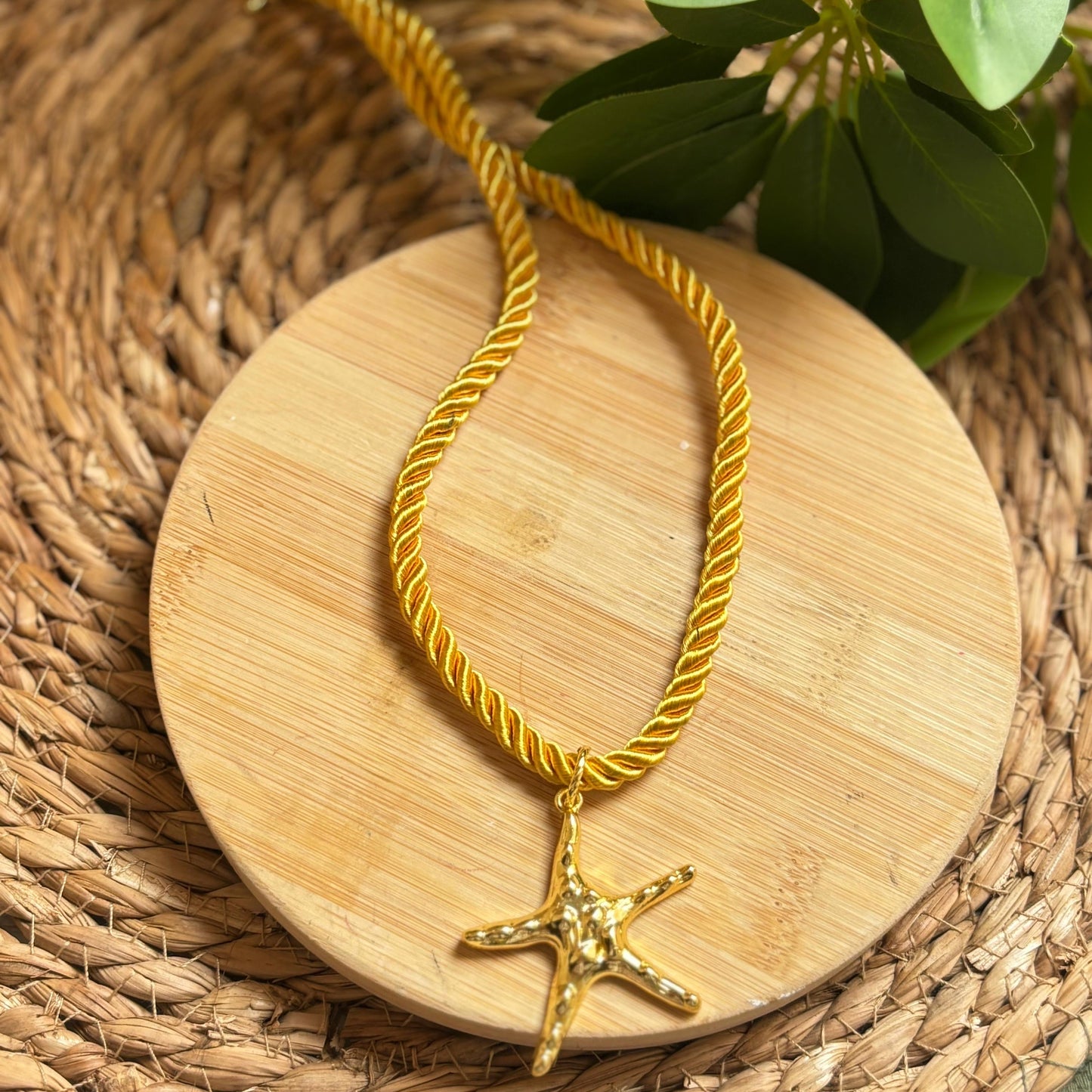 Gold necklace with a starfish pendant on a wooden coaster with greenery in the background