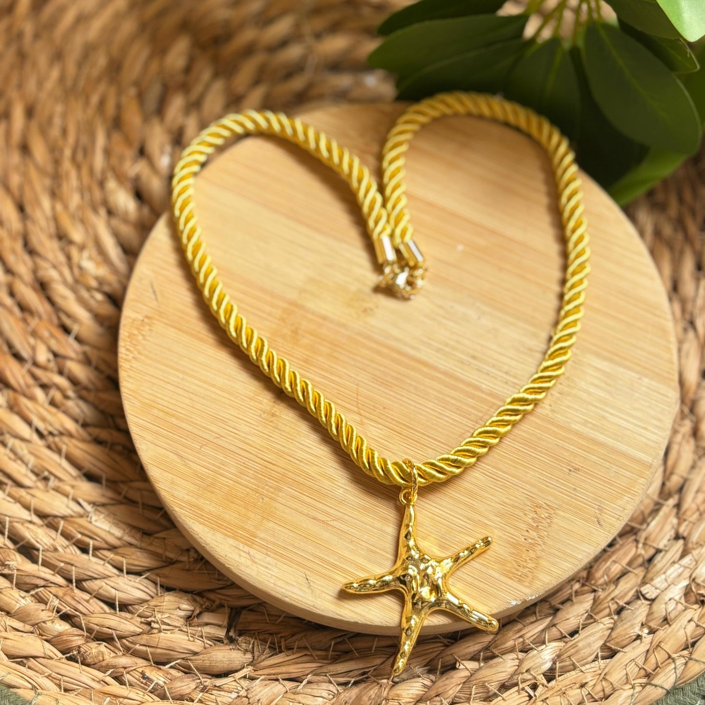 Gold necklace with a starfish pendant on a wooden heart-shaped coaster.