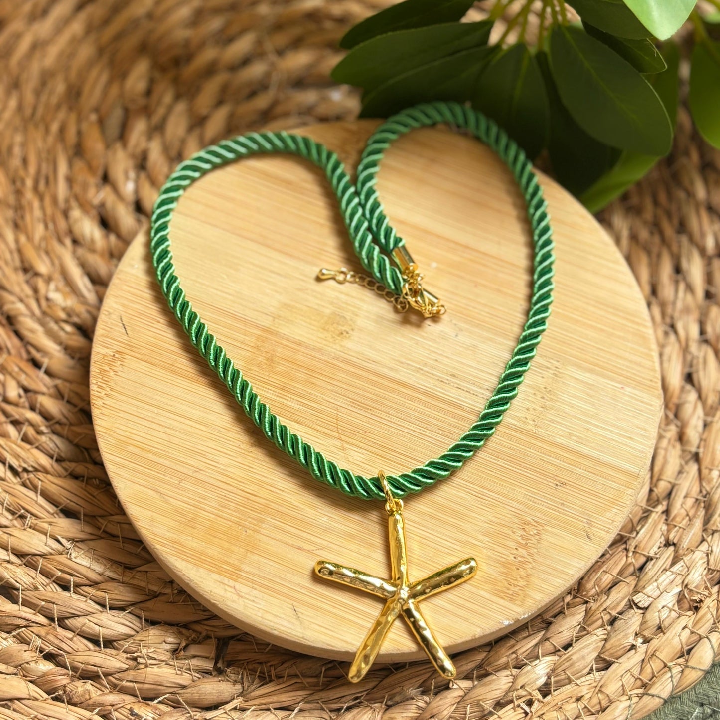 Green rope necklace with a gold starfish pendant on a wooden coaster.