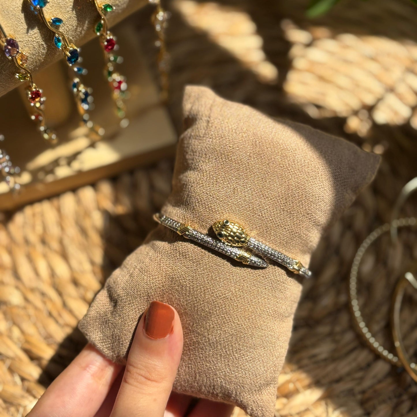 Bracelet on a brown fabric pad held by a hand, with a woven surface and plant in the background