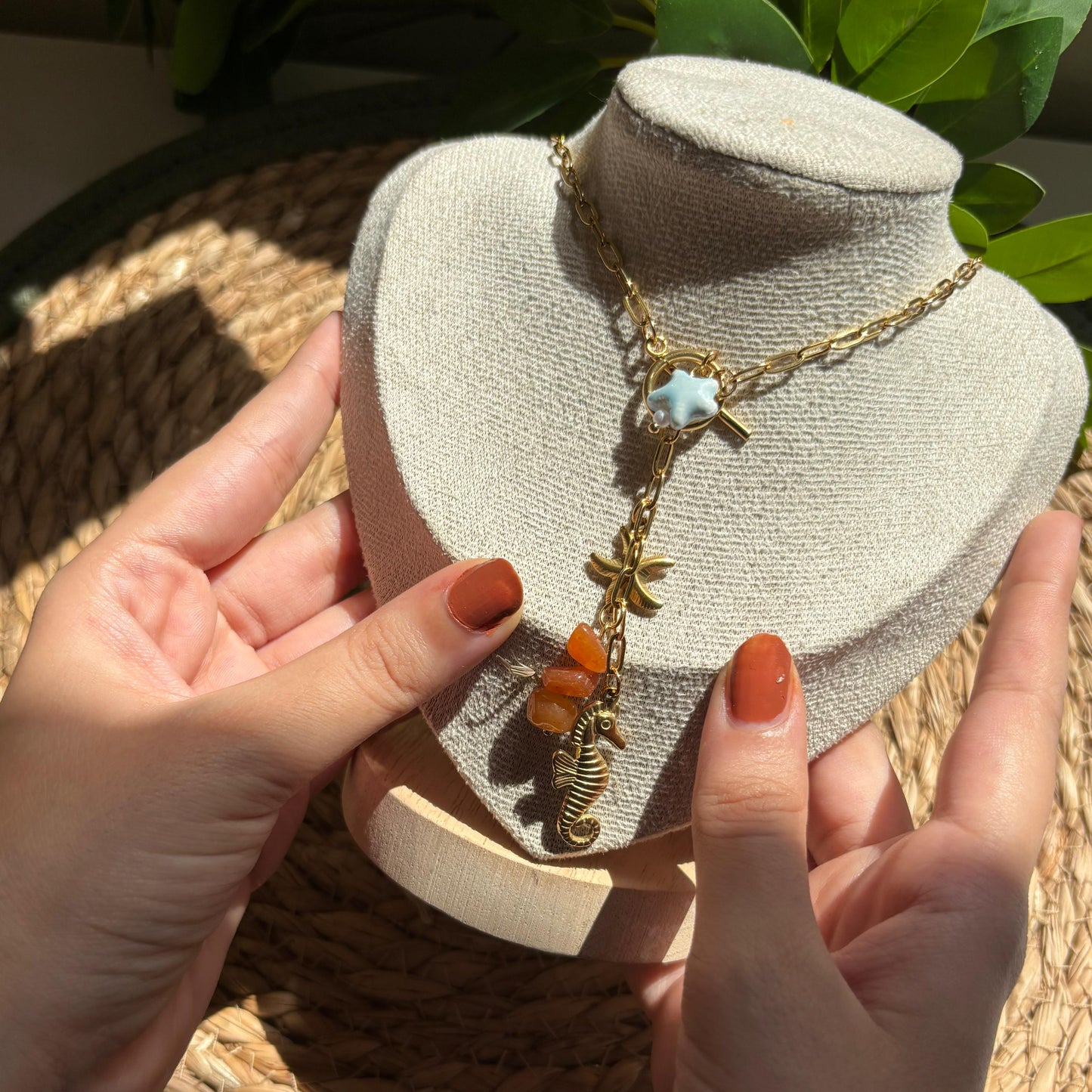 Gold necklace with orange beads on a mannequin bust held by hands with red nail polish.